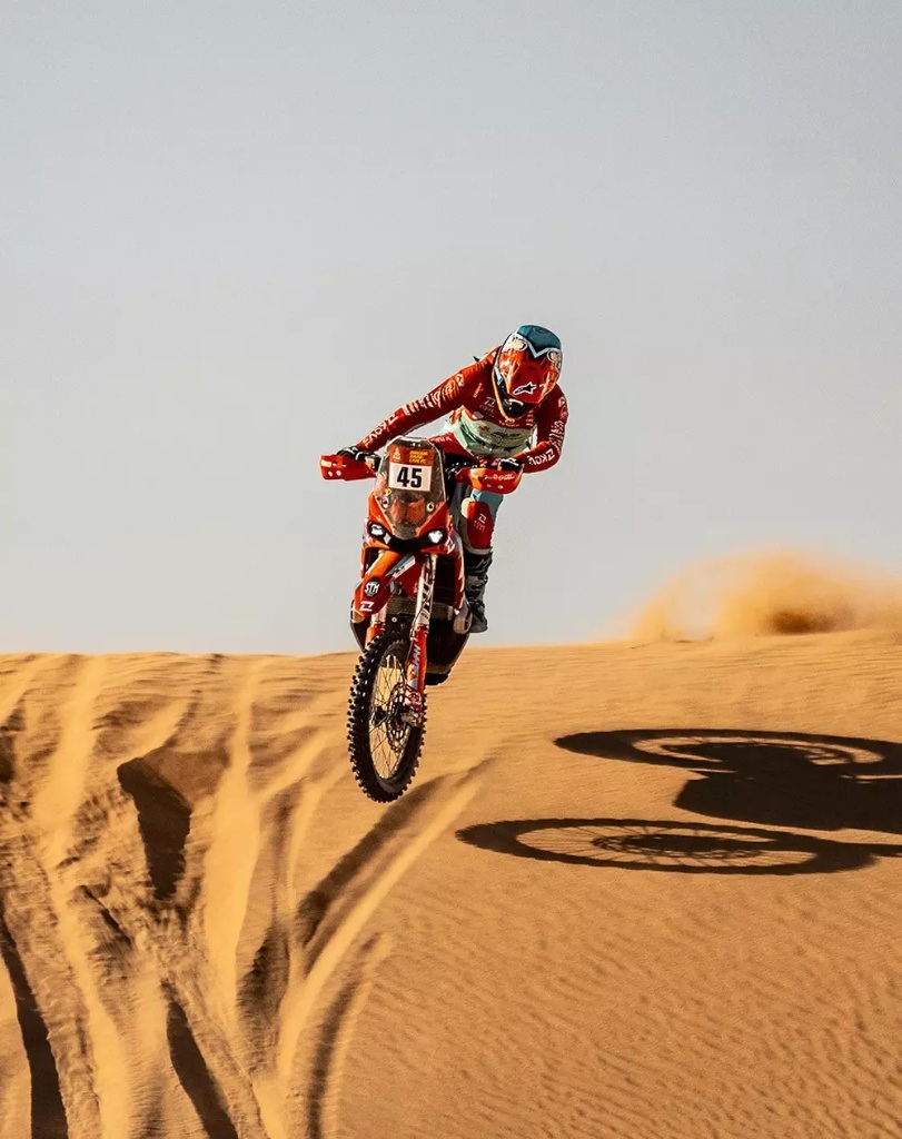Rider standing on KOVE rally bike jumping in desert sand